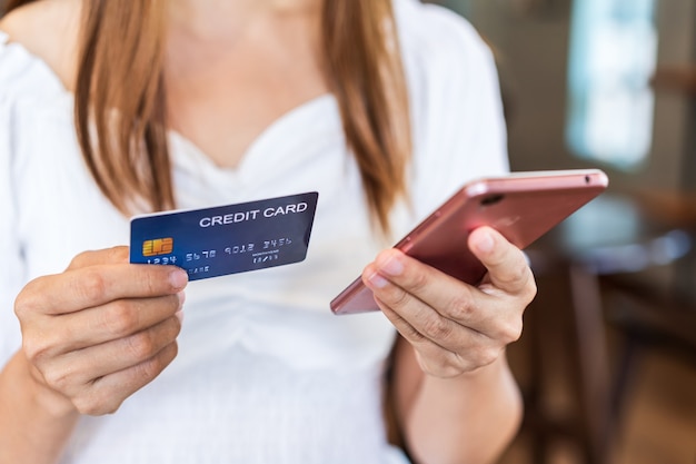 Giovane donna che tiene una carta di credito e utilizza lo smartphone per effettuare acquisti di pagamento online nel ristorante