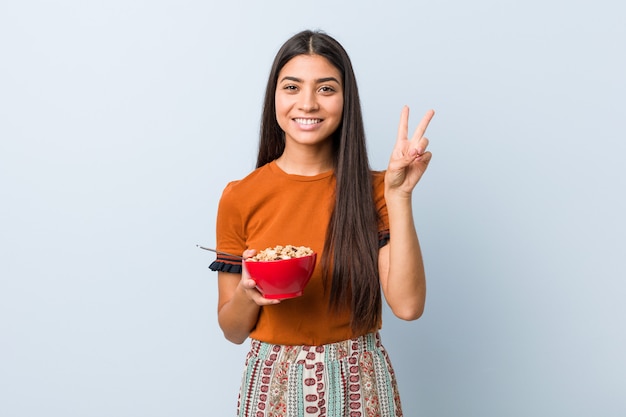 Giovane donna che tiene una ciotola di cereali che mostra il numero due con le dita.