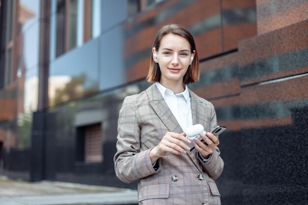 Giovane donna che tiene una custodia di cuffie wireless e smartphone in città