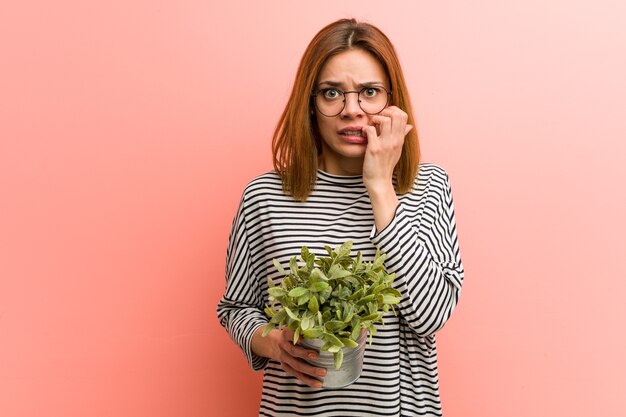 Giovane donna che tiene una pianta che morde le unghie, nervosa e molto ansiosa.