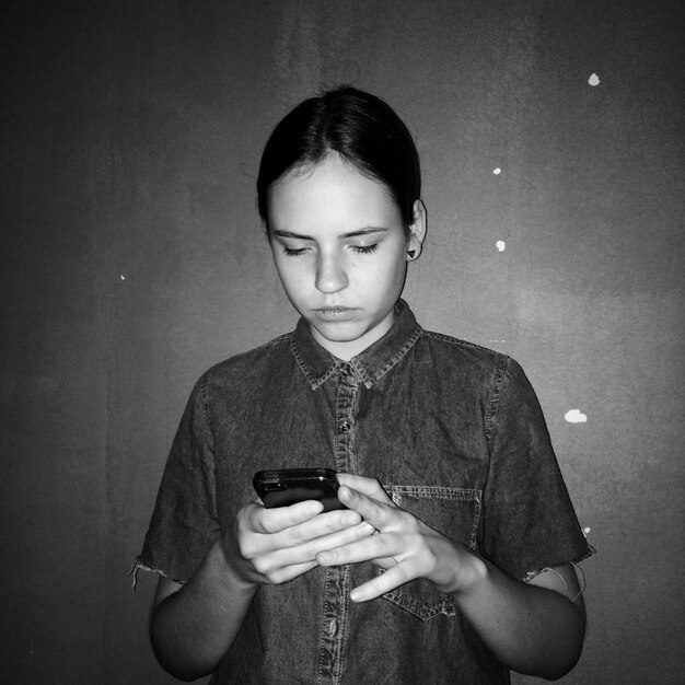 Giovane donna che usa il cellulare contro il muro