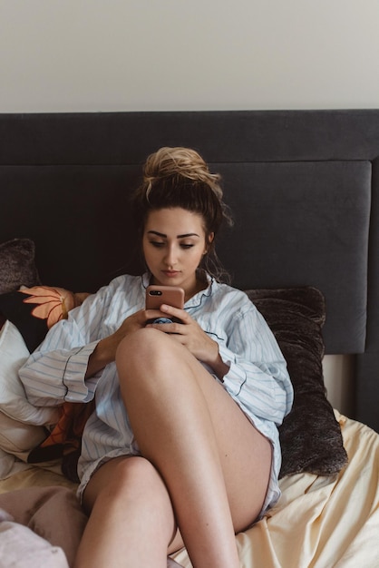 Giovane donna che usa il cellulare mentre è seduta a letto a casa