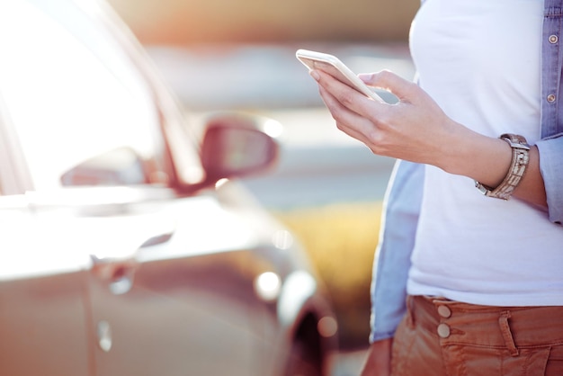 Giovane donna che usa il suo telefono per strada accanto alla sua auto