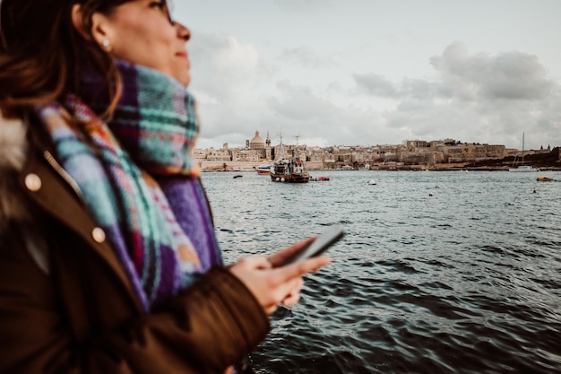 Giovane donna che usa il telefono cellulare sul mare contro il cielo