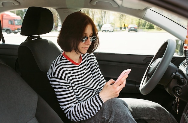 Giovane donna che usa lo smartphone seduta in macchina