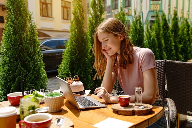 Giovane donna che utilizza computer portatile in un caffè su una terrazza estiva