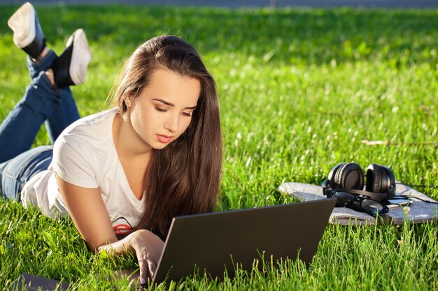 Giovane donna che utilizza computer portatile nel parco sdraiato sull'erba verde concetto di attività per il tempo libero
