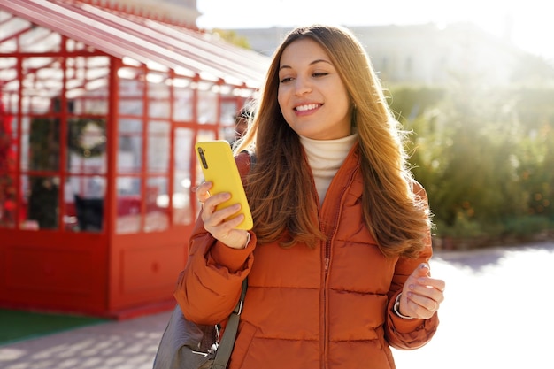 Giovane donna che utilizza il telefono a piedi in città in una soleggiata giornata invernale
