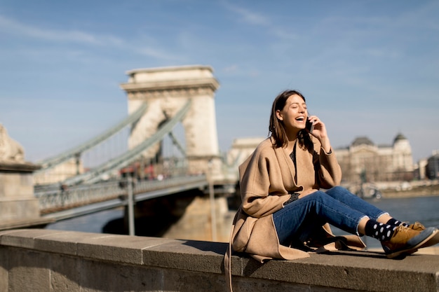 Giovane donna che utilizza il telefono cellulare con il ponte a catena a fondo a Budapest