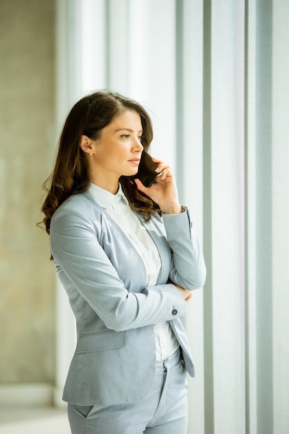 Giovane donna che utilizza il telefono cellulare dalla finestra dell'ufficio