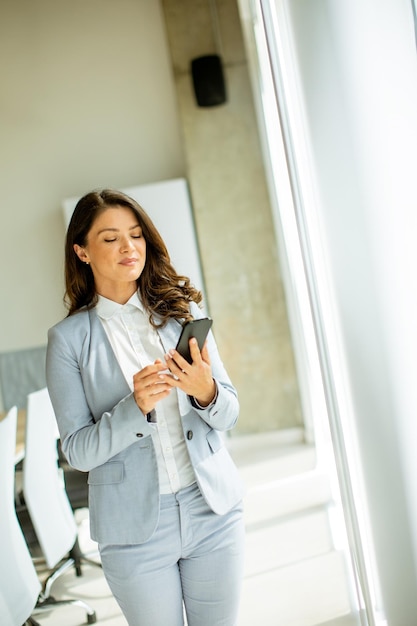 Giovane donna che utilizza il telefono cellulare dalla finestra dell'ufficio