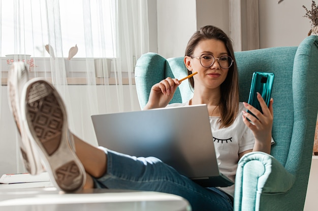 Giovane donna che utilizza il telefono cellulare e il computer portatile per lavorare a casa