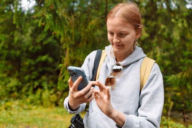 Giovane donna che utilizza il telefono cellulare mentre si cammina nei boschi durante l'escursione estiva in montagna Escursionismo orientamento turistico sul terreno utilizzando una mappa online un'applicazione in uno smartphone