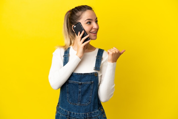 Giovane donna che utilizza il telefono cellulare su sfondo giallo isolato che punta al lato per presentare un prodotto