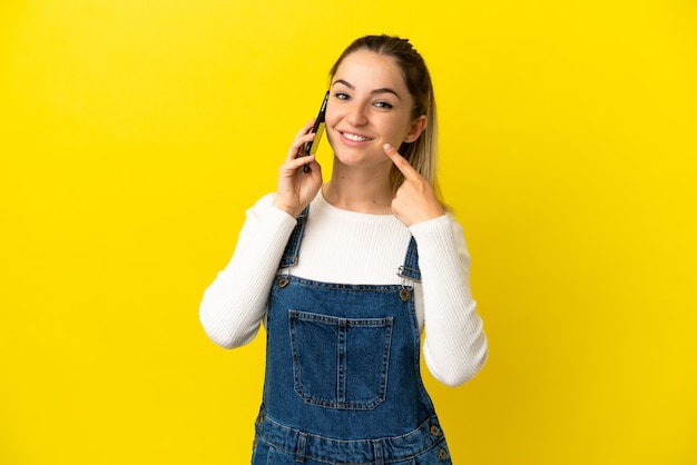 Giovane donna che utilizza il telefono cellulare su sfondo giallo isolato dando un gesto di pollice in alto