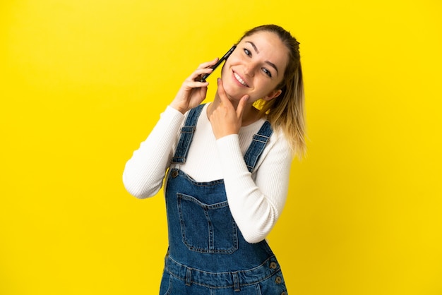 Giovane donna che utilizza il telefono cellulare su sfondo giallo isolato felice e sorridente