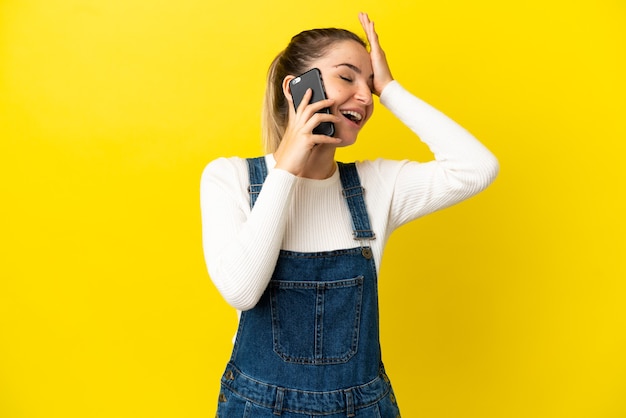 Giovane donna che utilizza il telefono cellulare su sfondo giallo isolato sorridendo molto