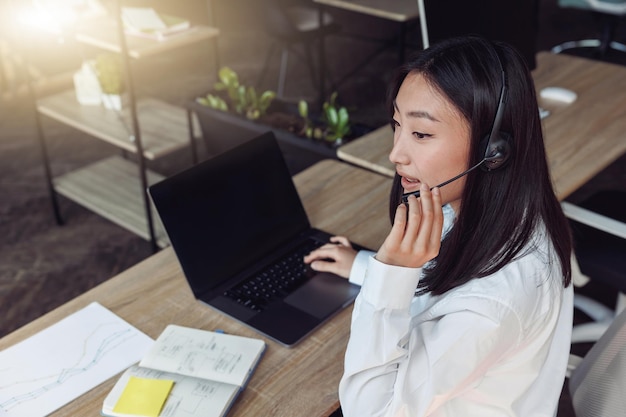 Giovane donna che utilizza l'auricolare e il computer mentre parla con i clienti online