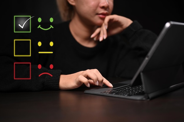 Giovane donna che utilizza la tavoletta del computer per selezionare l'icona della faccina sorridente per valutare il prodotto e il servizio