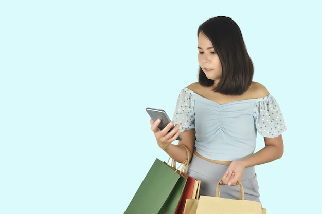 Giovane donna che utilizza smartphone e tiene in mano le borse della spesa Concetto di app per lo shopping online