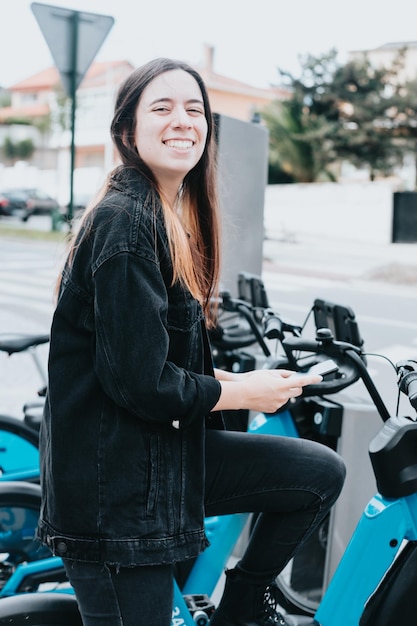 Giovane donna che utilizza un sistema urbano di supporto per biciclette a noleggio sorridente super felice durante il test della città europea delle biciclette con un trasporto verde per biciclette a noleggio