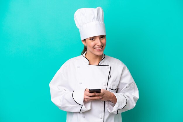 Giovane donna chef caucasica isolata su sfondo blu che invia un messaggio con il cellulare