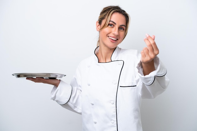 Giovane donna chef con vassoio isolato su sfondo bianco che fa gesto di denaro