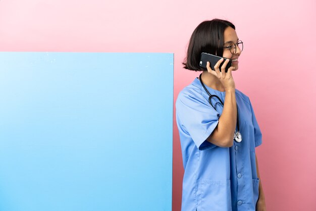 Giovane donna chirurgo di razza mista con un grande striscione sul muro isolato mantenendo una conversazione con il telefono cellulare con qualcuno