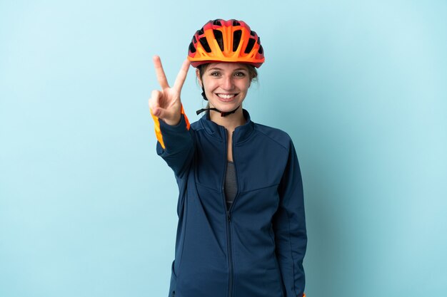 Giovane donna ciclista isolata sull'azzurro che sorride e che mostra il segno di vittoria