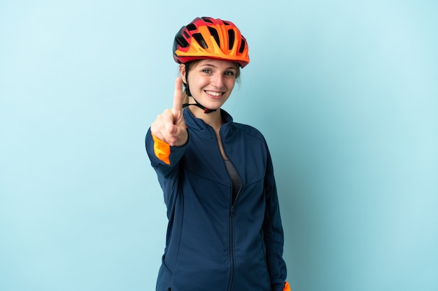 Giovane donna ciclista sulla rappresentazione blu e alzando un dito