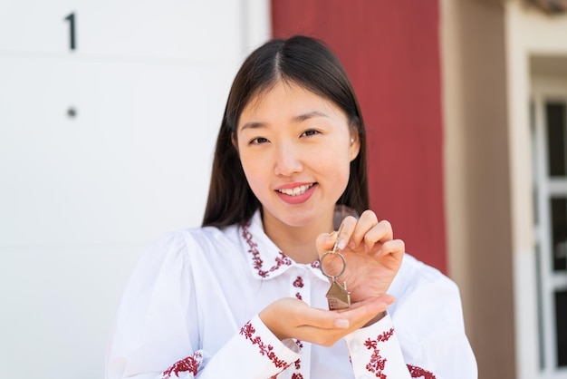Giovane donna cinese all'aperto che tiene le chiavi di casa con felice espressione