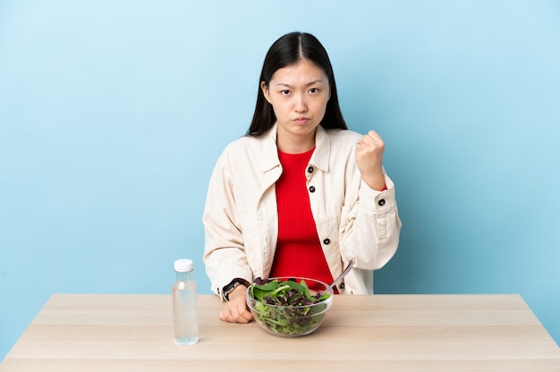 Giovane donna cinese che mangia un'insalata con l'espressione infelice