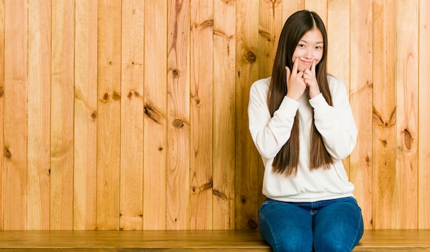 Giovane donna cinese che si siede su un posto di legno che dubita fra due opzioni.