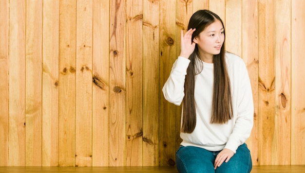 Giovane donna cinese che si siede su un posto di legno che prova ad ascoltare un gossip.