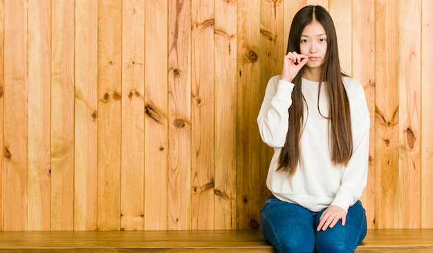 Giovane donna cinese che si siede su un posto di legno con le dita sulle labbra che tengono un segreto.