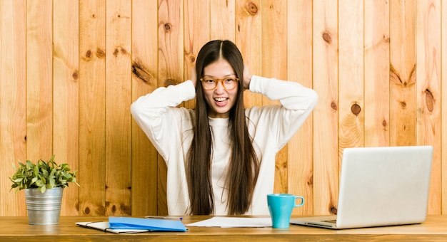 Giovane donna cinese che studia sulla sua scrivania che copre le orecchie con le mani cercando di non sentire un suono troppo forte.