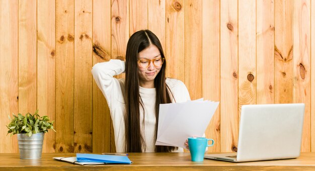 Giovane donna cinese che studia sulla sua scrivania toccando la parte posteriore della testa, pensando e facendo una scelta.