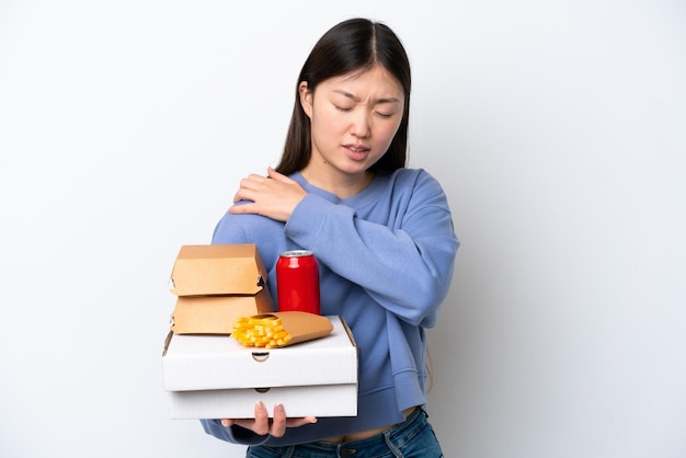 Giovane donna cinese che tiene fast food isolato su sfondo bianco che soffre di dolore alla spalla per aver fatto uno sforzo