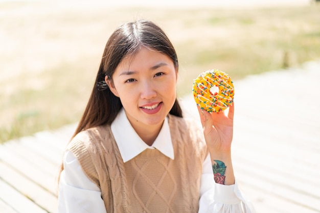 Giovane donna cinese che tiene una ciambella all'aperto che sorride molto