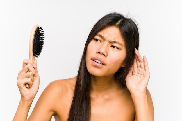 Giovane donna cinese che tiene una spazzola per capelli che prova ad ascoltare un gossip.