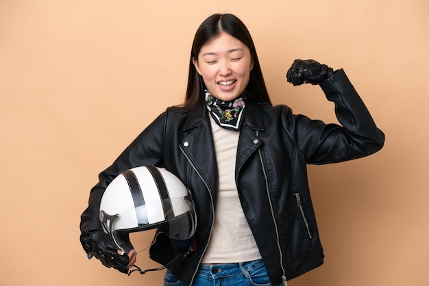 Giovane donna cinese con un casco da motociclista isolato su sfondo beige che fa un forte gesto