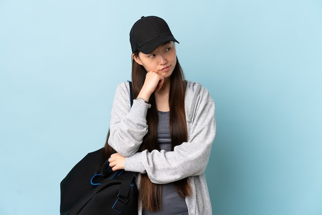 Giovane donna cinese di sport con borsa sportiva sopra la parete blu isolata con espressione stanca e annoiata