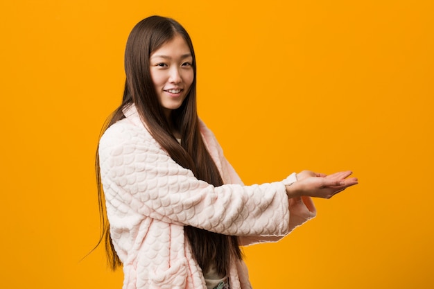 Giovane donna cinese in pigiama che tiene uno spazio della copia su una palma.