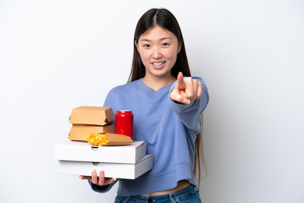 Giovane donna cinese in possesso di fast food isolato su sfondo bianco che punta davanti con l'espressione felice