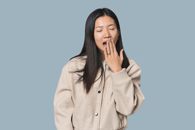 Giovane donna cinese in studio sbadigliando mostrando un gesto stanco che copre la bocca con la mano