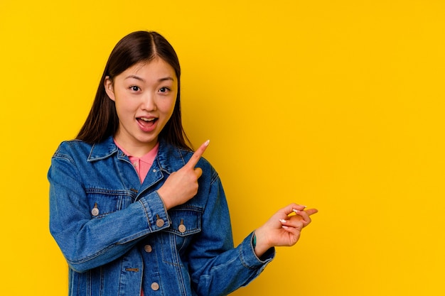 Giovane donna cinese isolata su giallo eccitato che punta con gli indici di distanza.