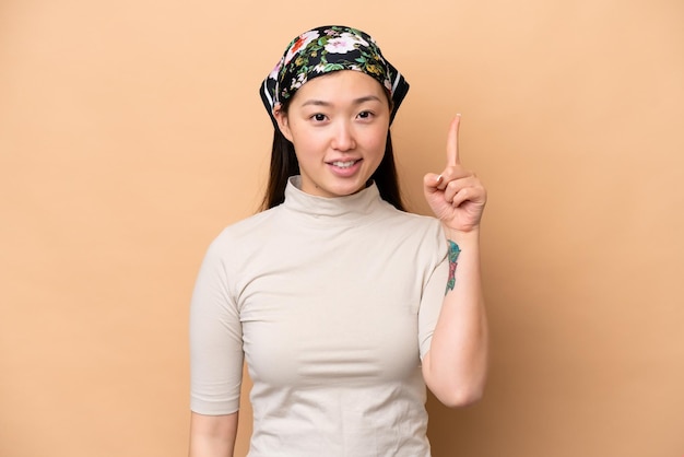 Giovane donna cinese isolata su sfondo beige che indica una grande idea