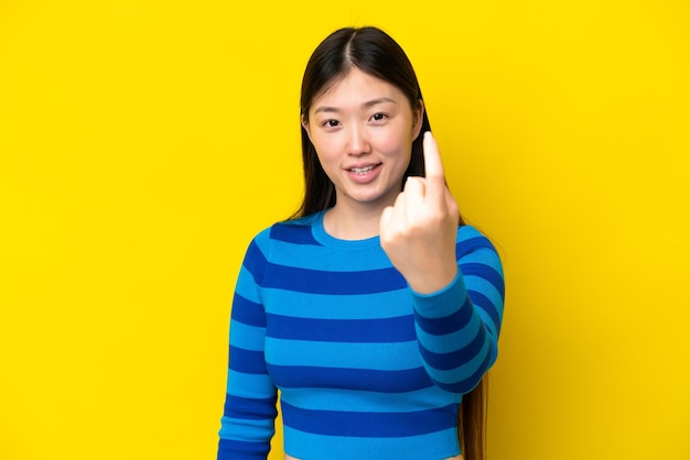 Giovane donna cinese isolata su sfondo giallo che fa il gesto in arrivo