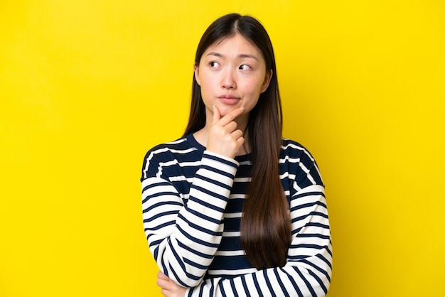 Giovane donna cinese isolata su sfondo giallo che ha dei dubbi