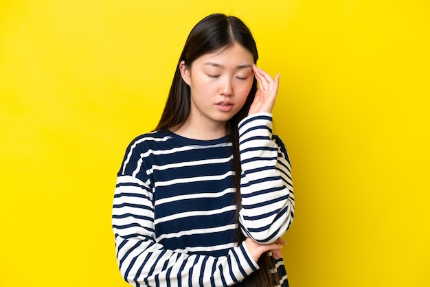 Giovane donna cinese isolata su sfondo giallo con mal di testa